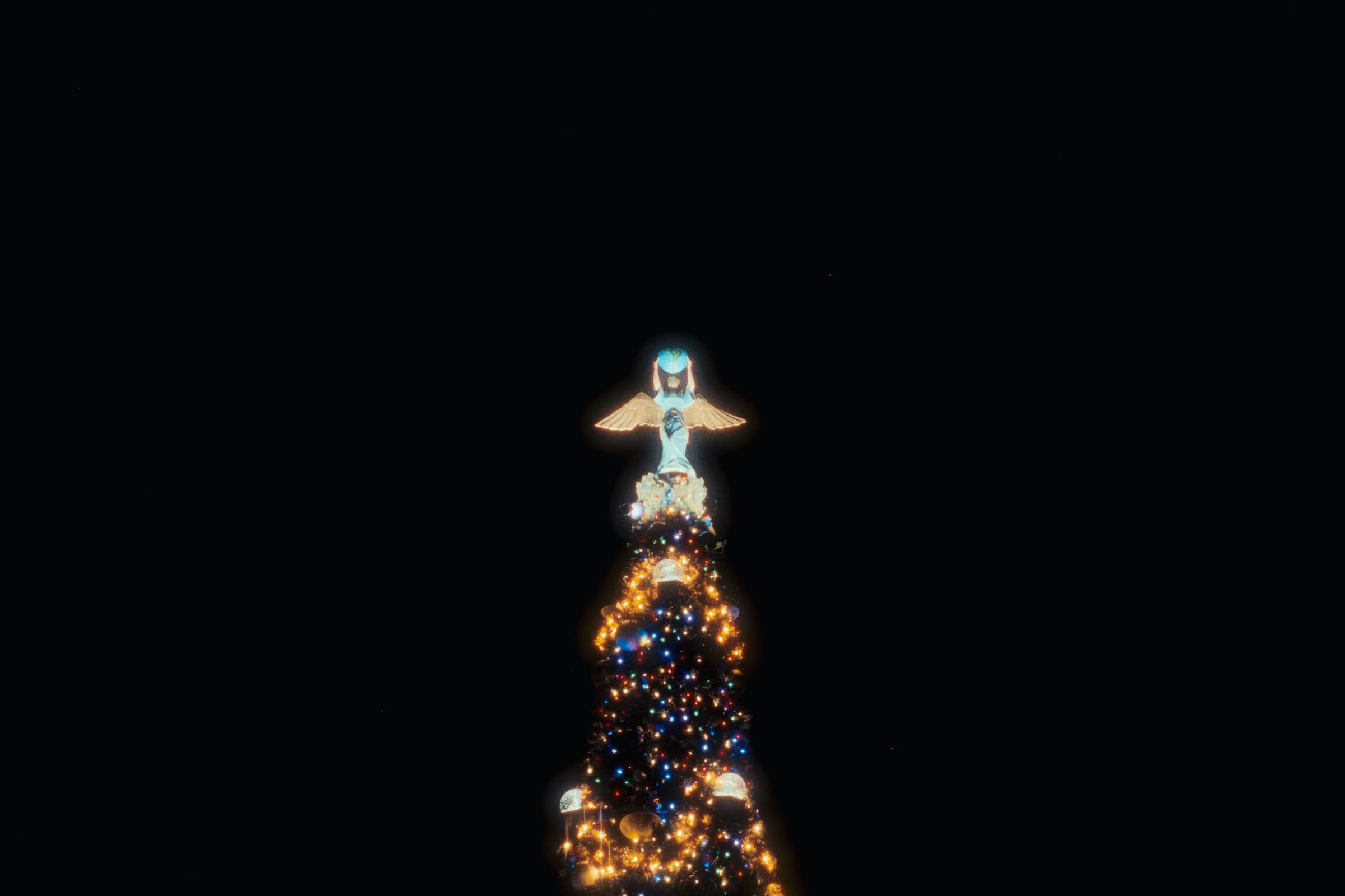 A tall Christmas tree with an angel topper against the night sky.