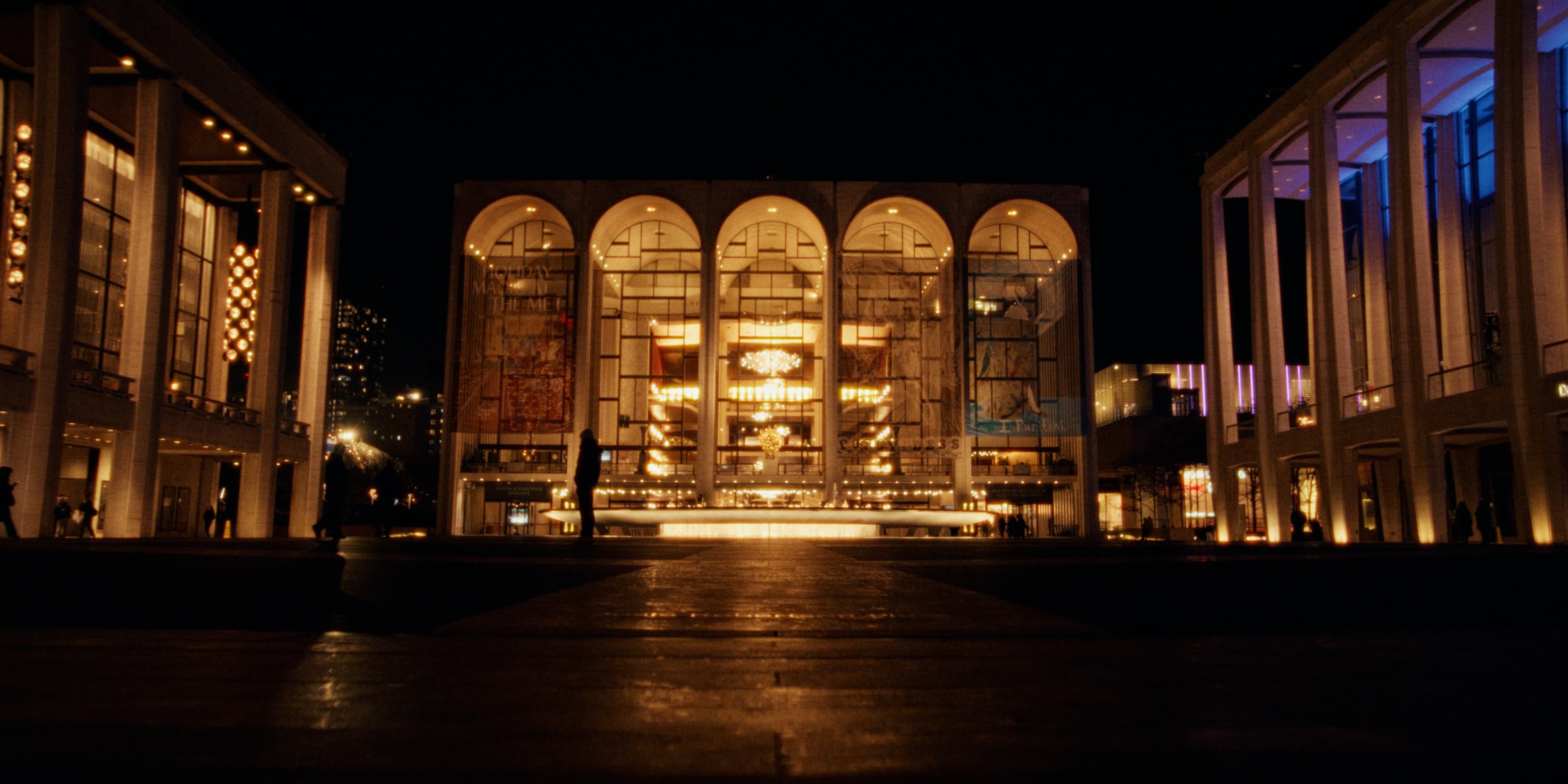 The Lincoln Center plaza at night with the Metropolitan Opera House glowing behind the fountain.