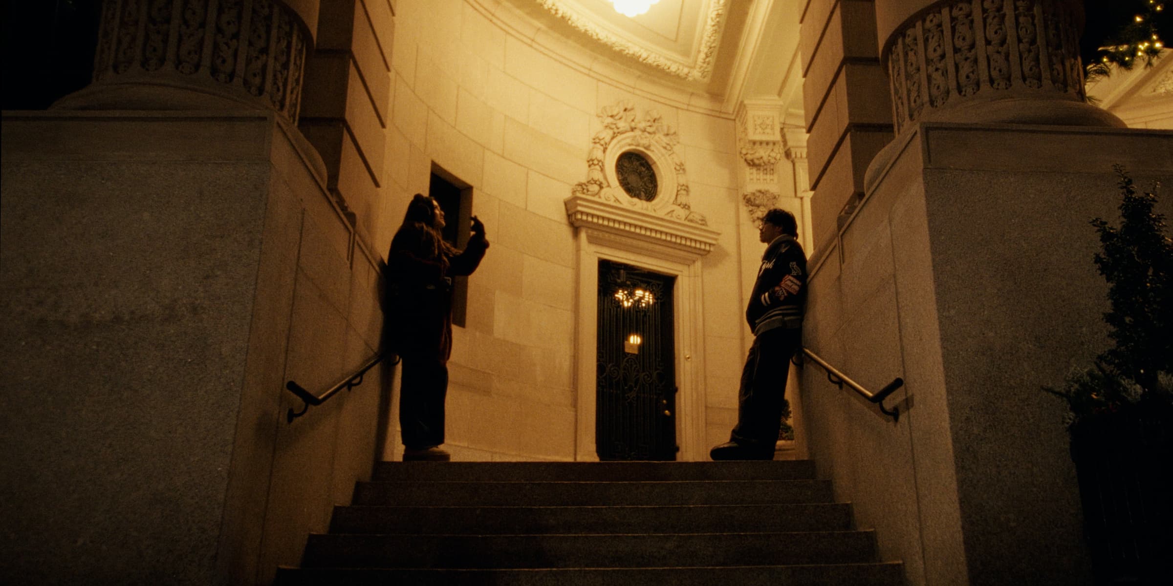 Andrew Amisola in I Could Write a Book about Christmas in New York City — Two friends stand on steps outside a grand stone building at night.