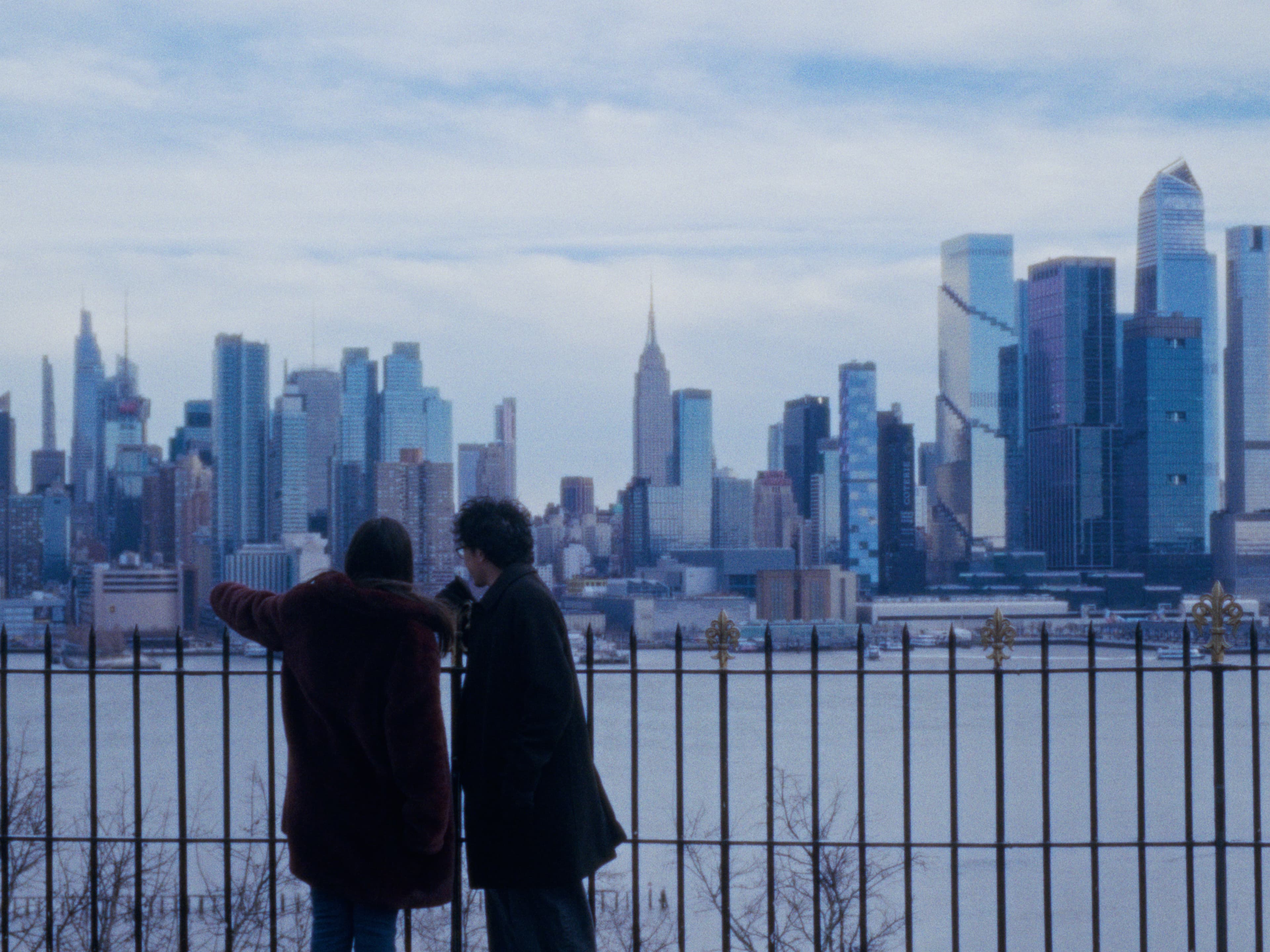 Two friends at a railing looking across the water toward the skyline.