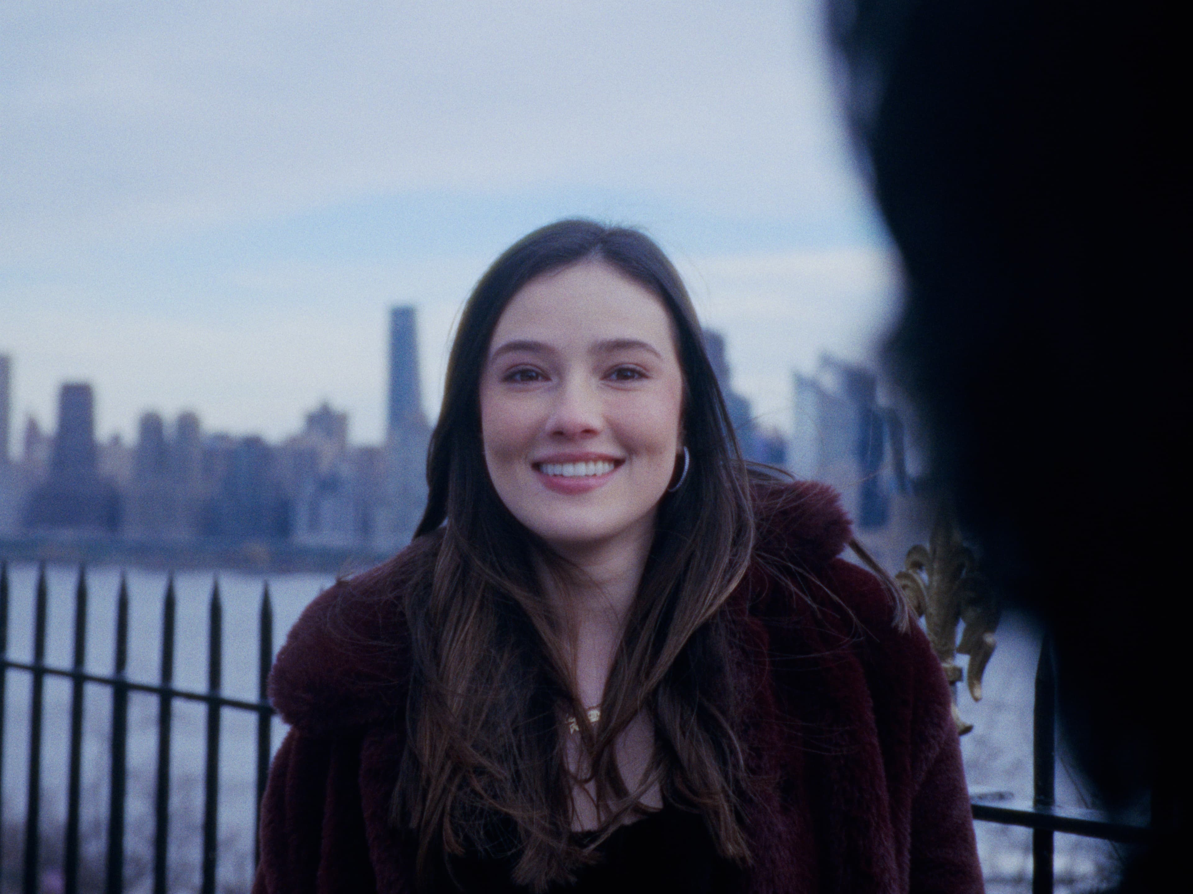 Juliana smiles at the camera with the skyline softly blurred behind her.
