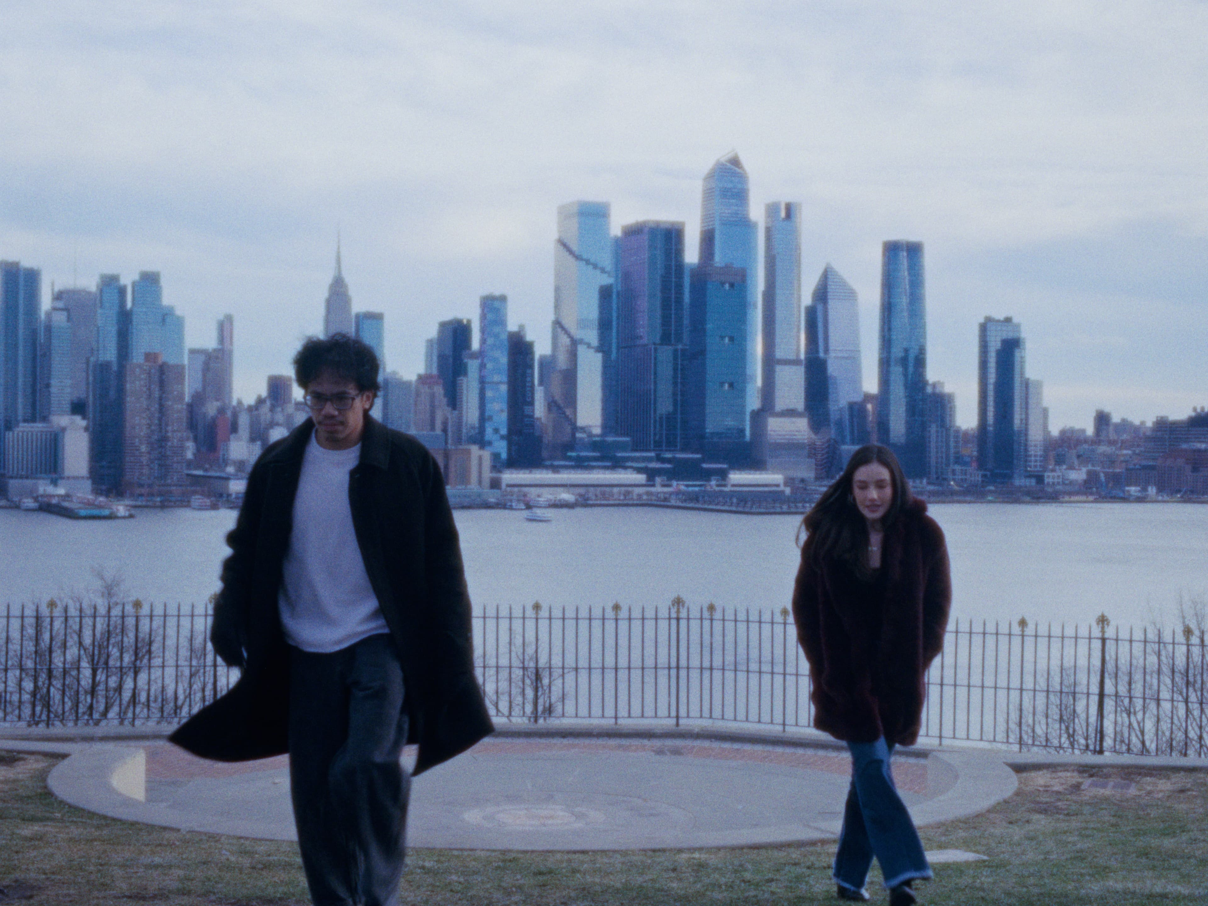 Andrew and Juliana walk across a grassy overlook with the skyline behind them.