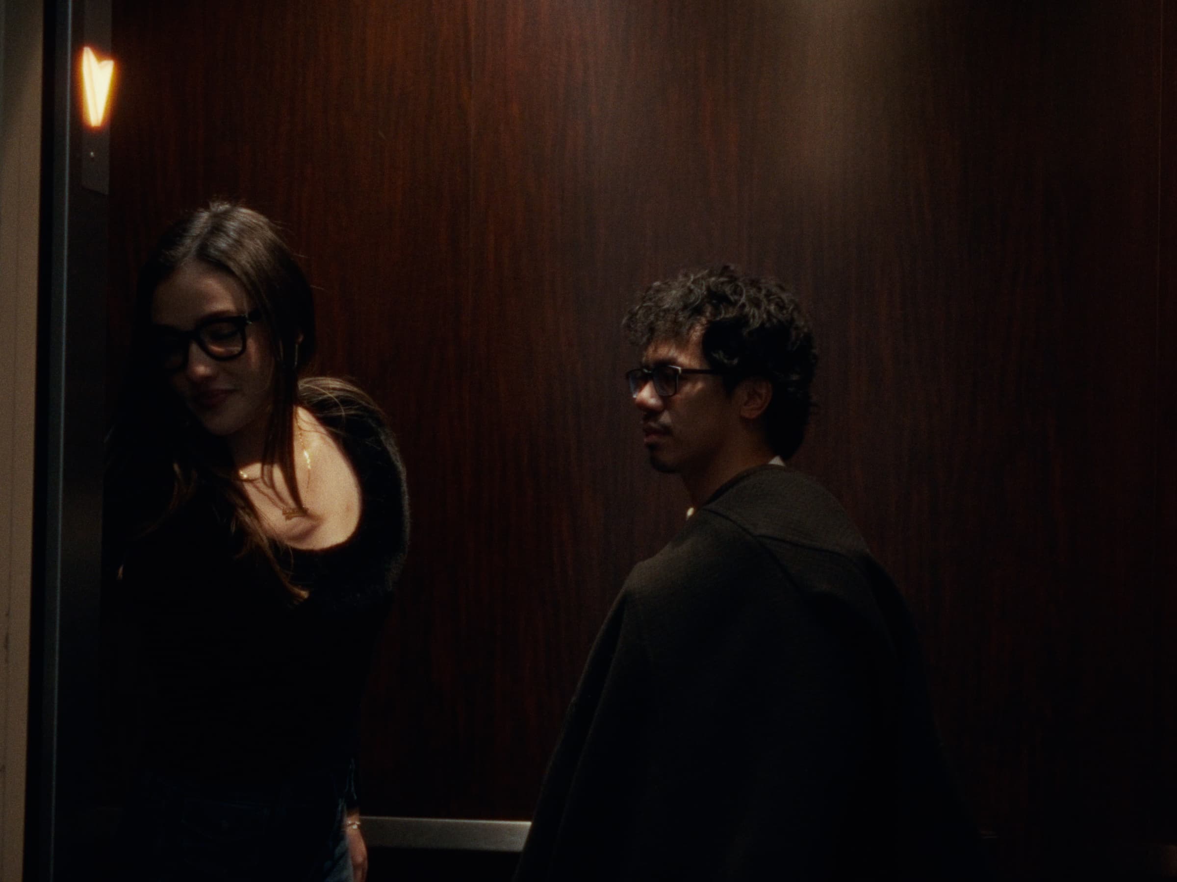 Andrew Amisola in December Blue — Two friends in a dim elevator with warm, wood-paneled walls.