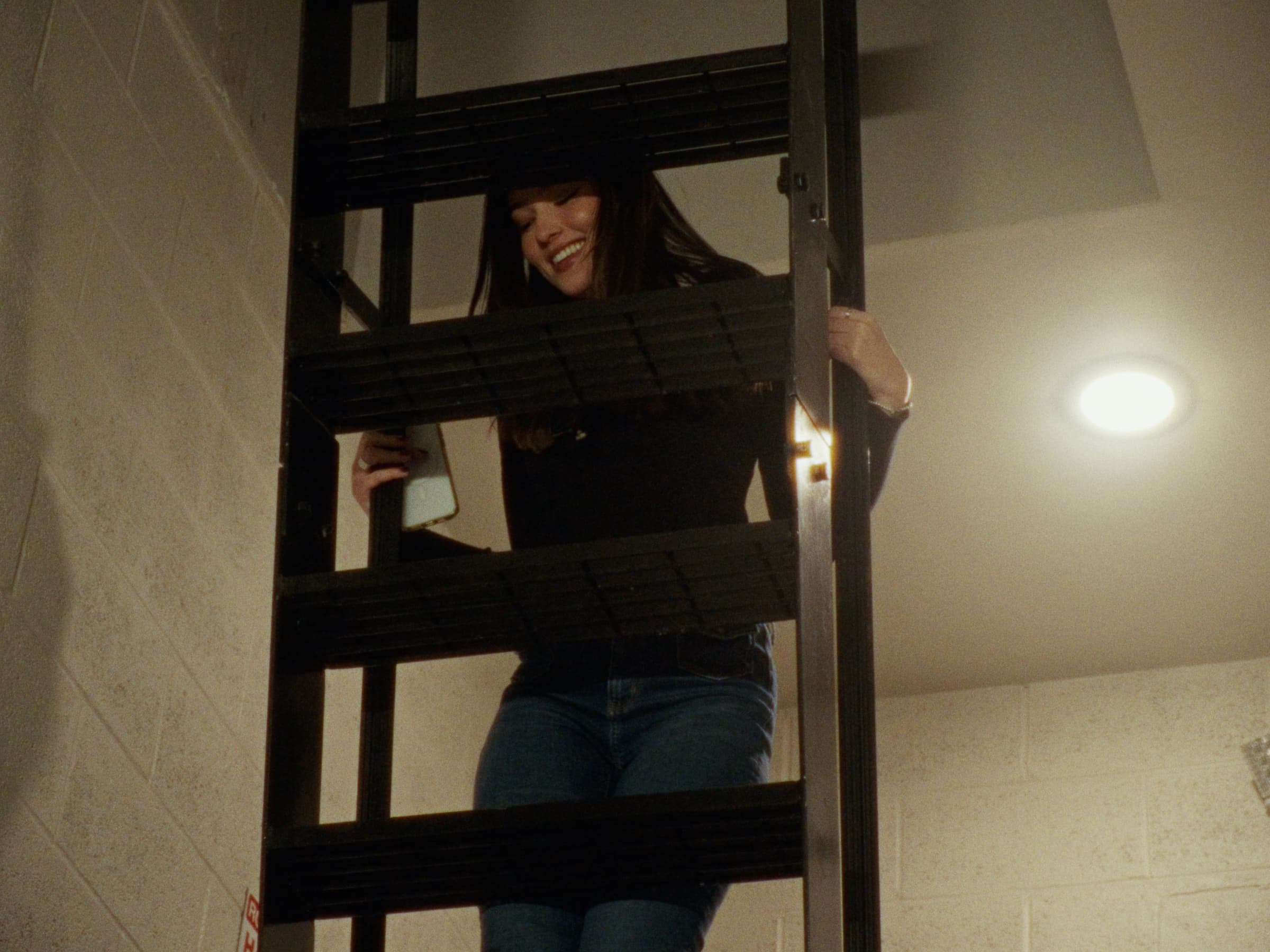 Juliana smiles while standing on a ladder in a softly lit interior.