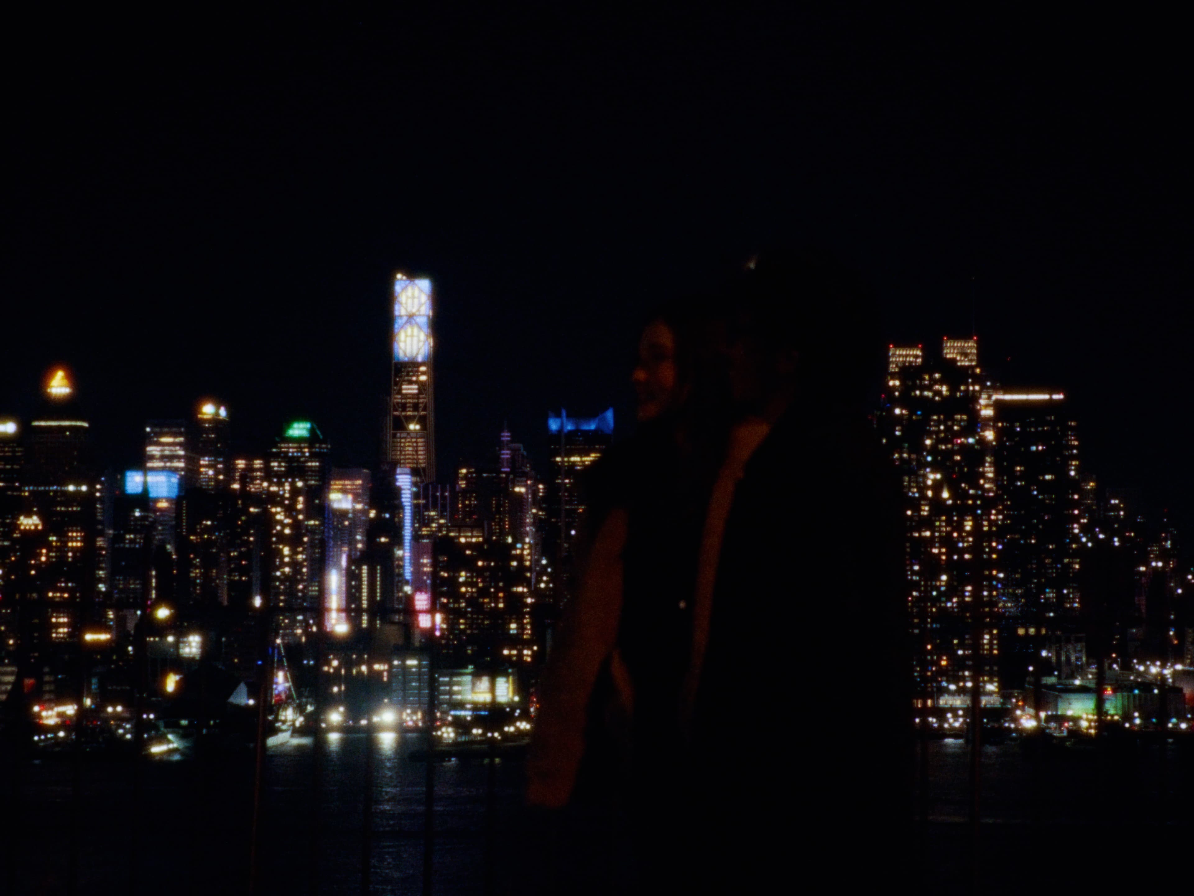 Two figures in silhouette before the New York skyline at night.