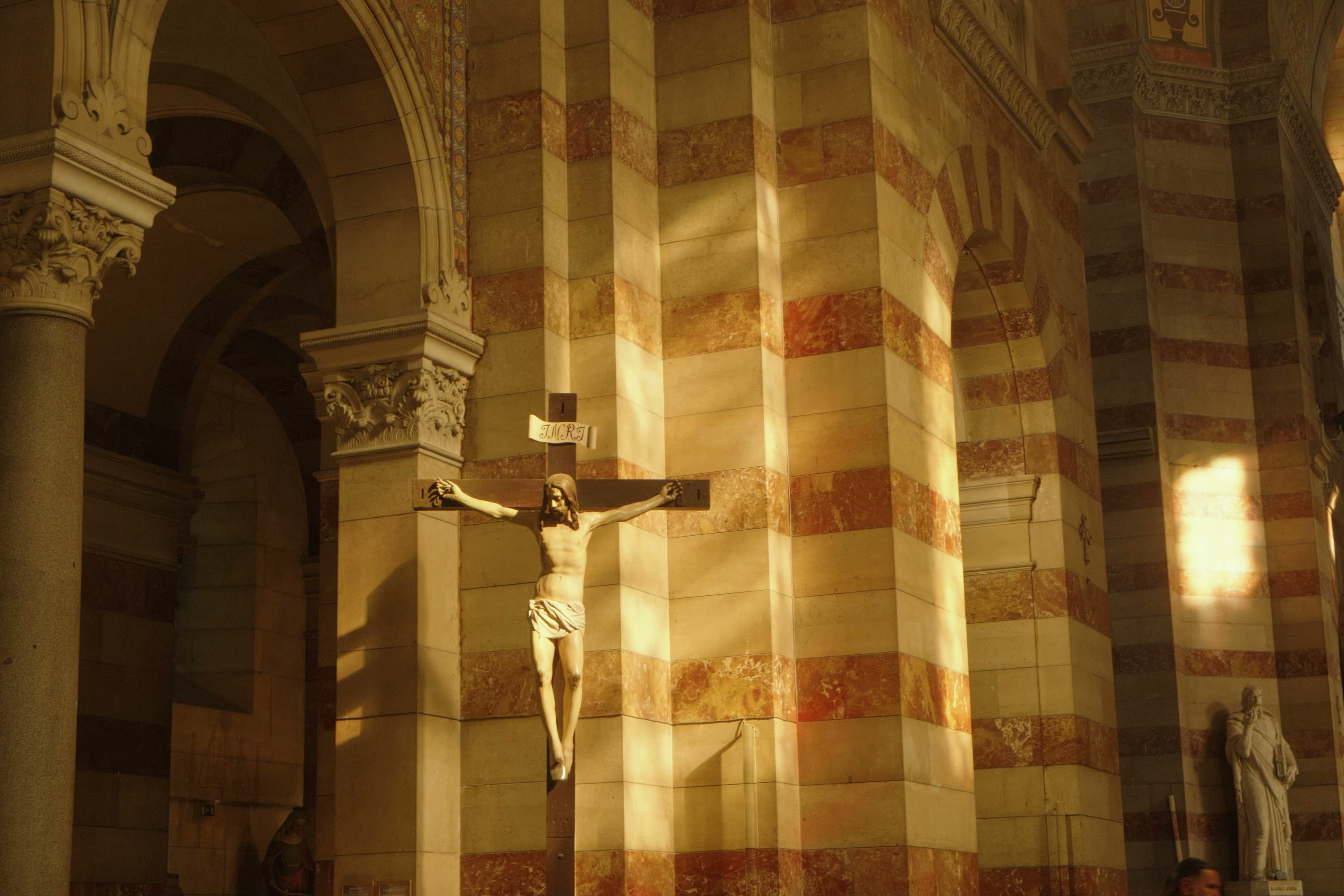 Interior of Marseille Cathedral with a crucifix and striped marble columns bathed in golden light.