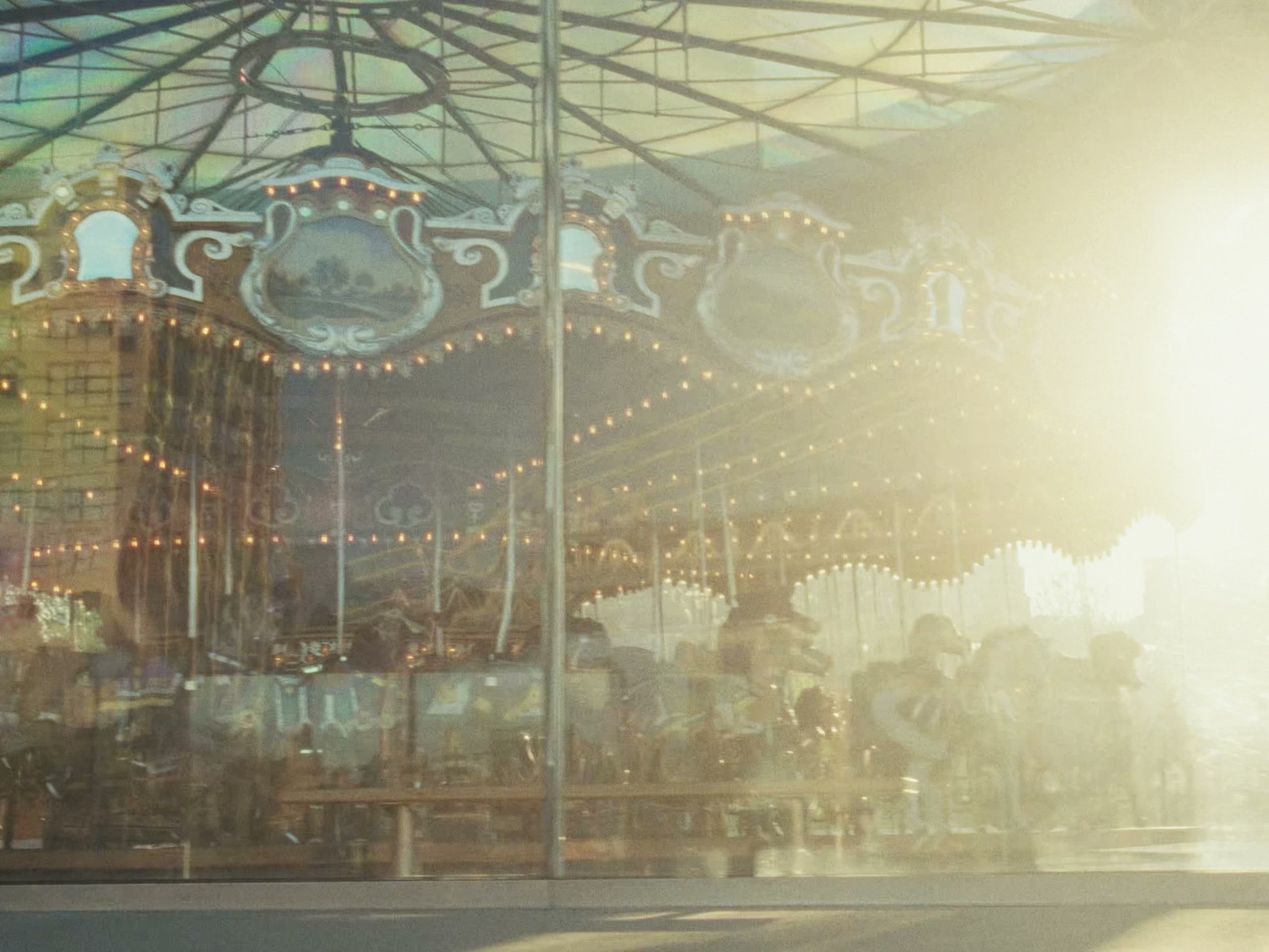Jane's Carousel viewed through its glass pavilion, strings of warm bulbs and gilded panels visible, a heavy blown-out sun flare covering the right half of the frame.