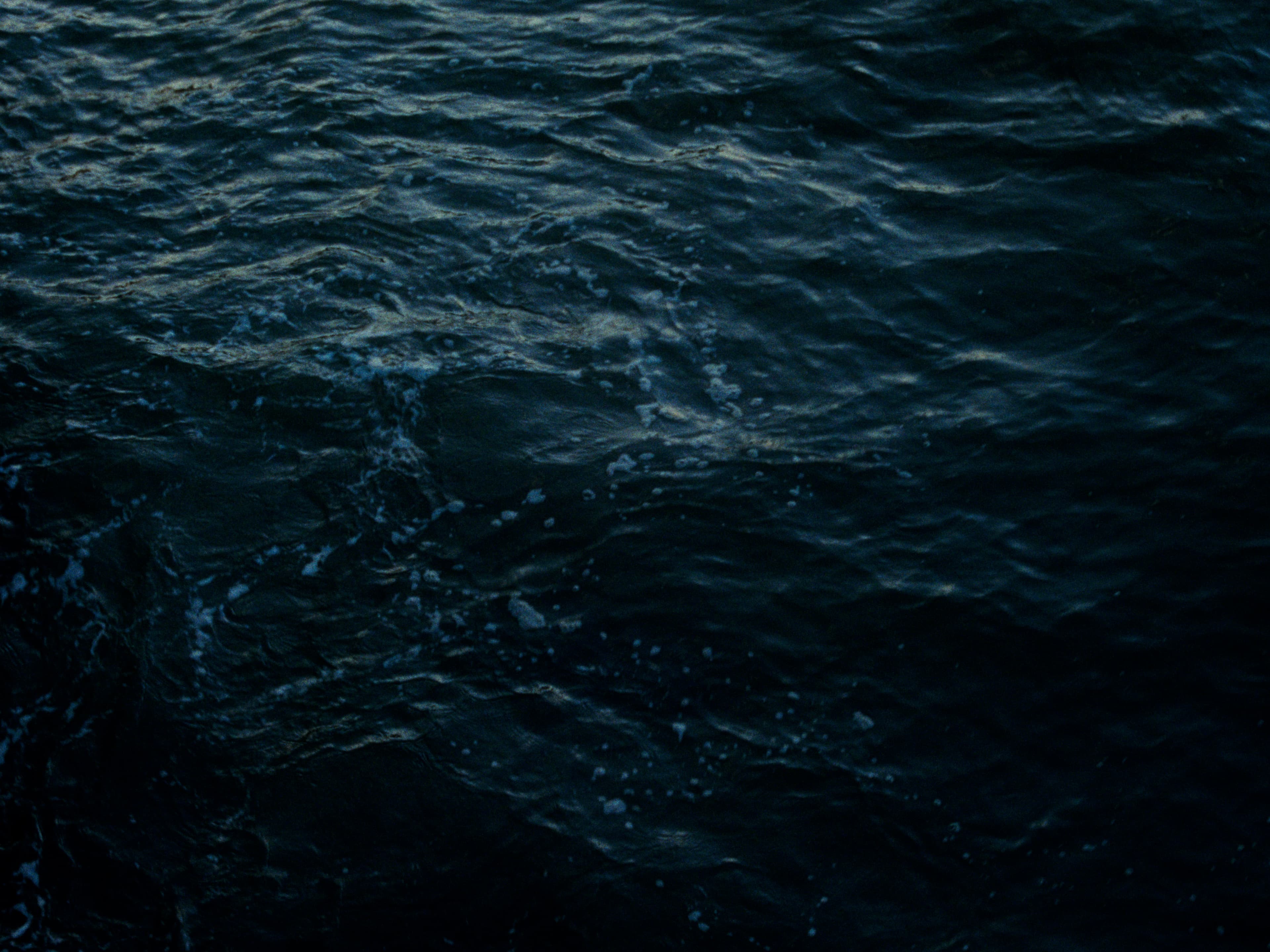 Tight view of dark East River water, small whitecaps and a spatter of spray catching the last light.
