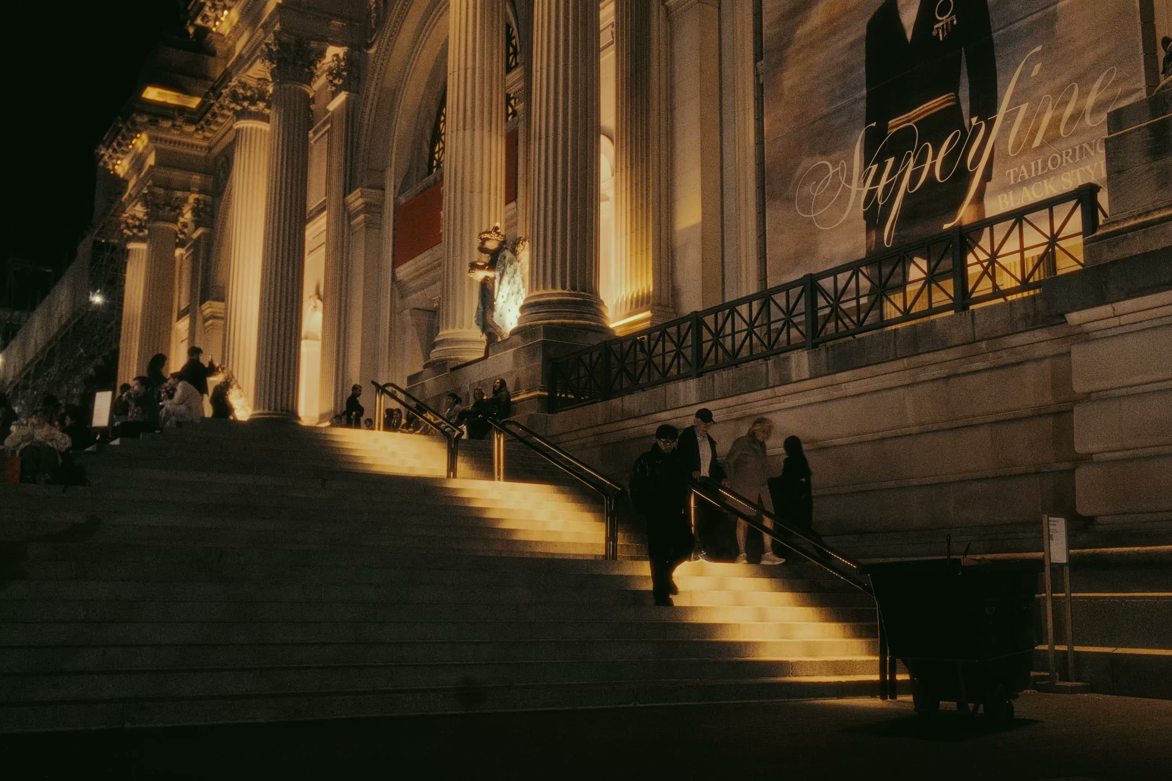 People ascending the Met's grand staircase at night under warm lighting.