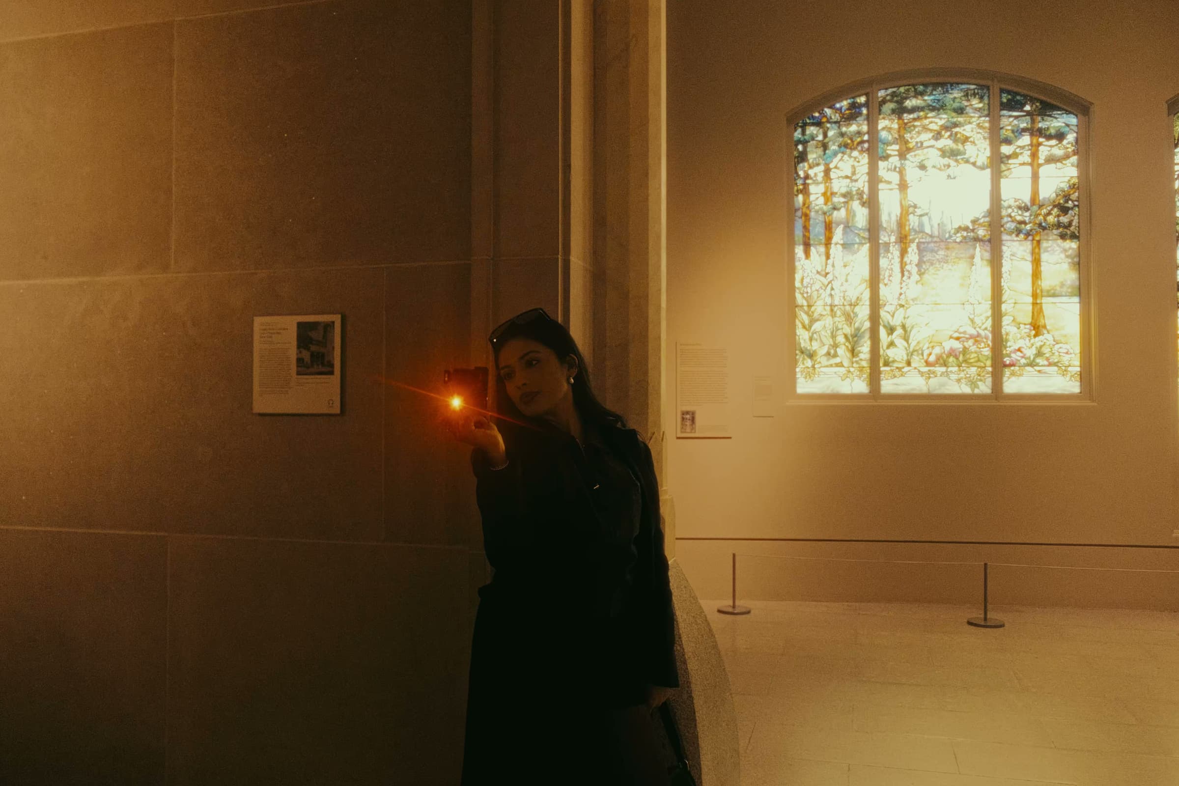 A woman photographing art near a Tiffany stained glass window.