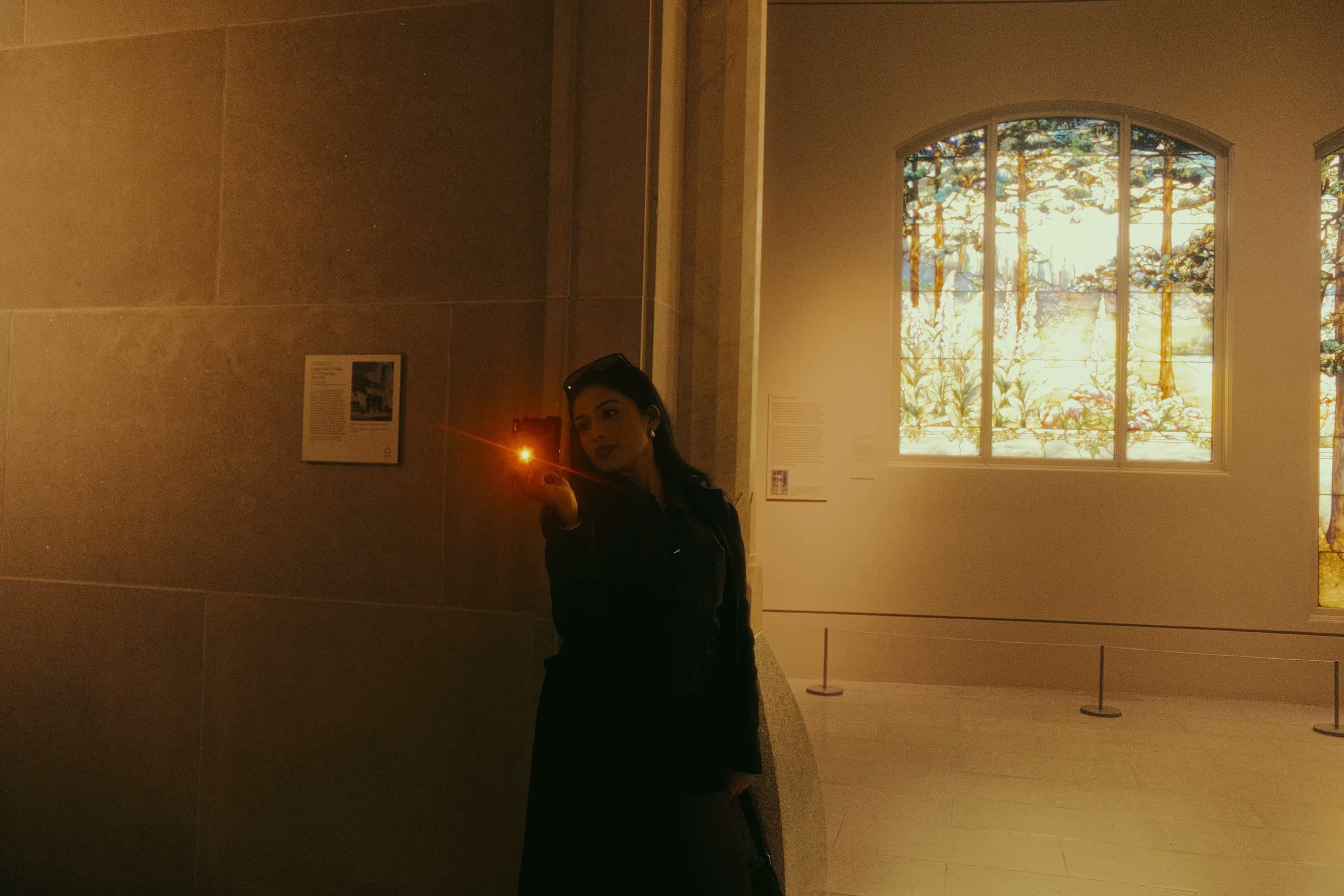 A woman photographing art near a Tiffany stained glass window.