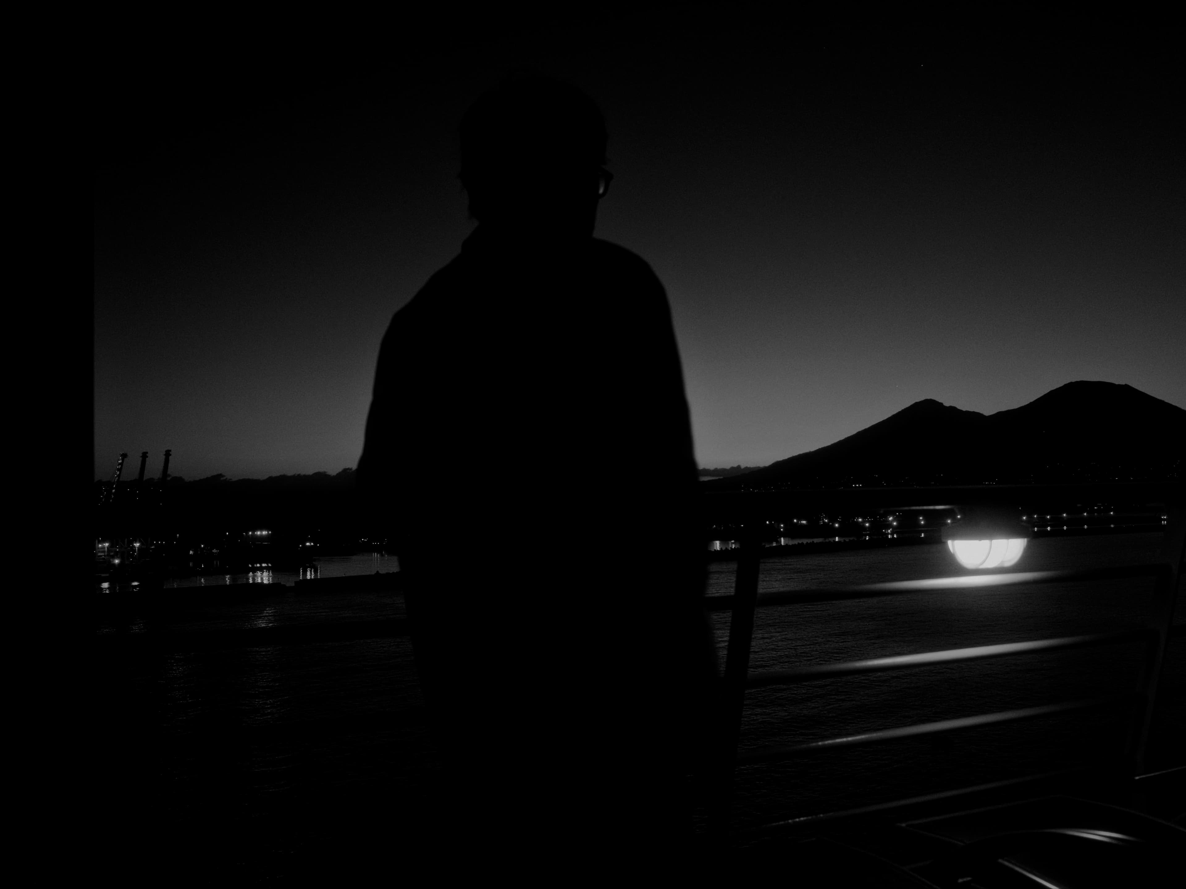 A silhouetted figure stands by a railing overlooking the sea at night.
