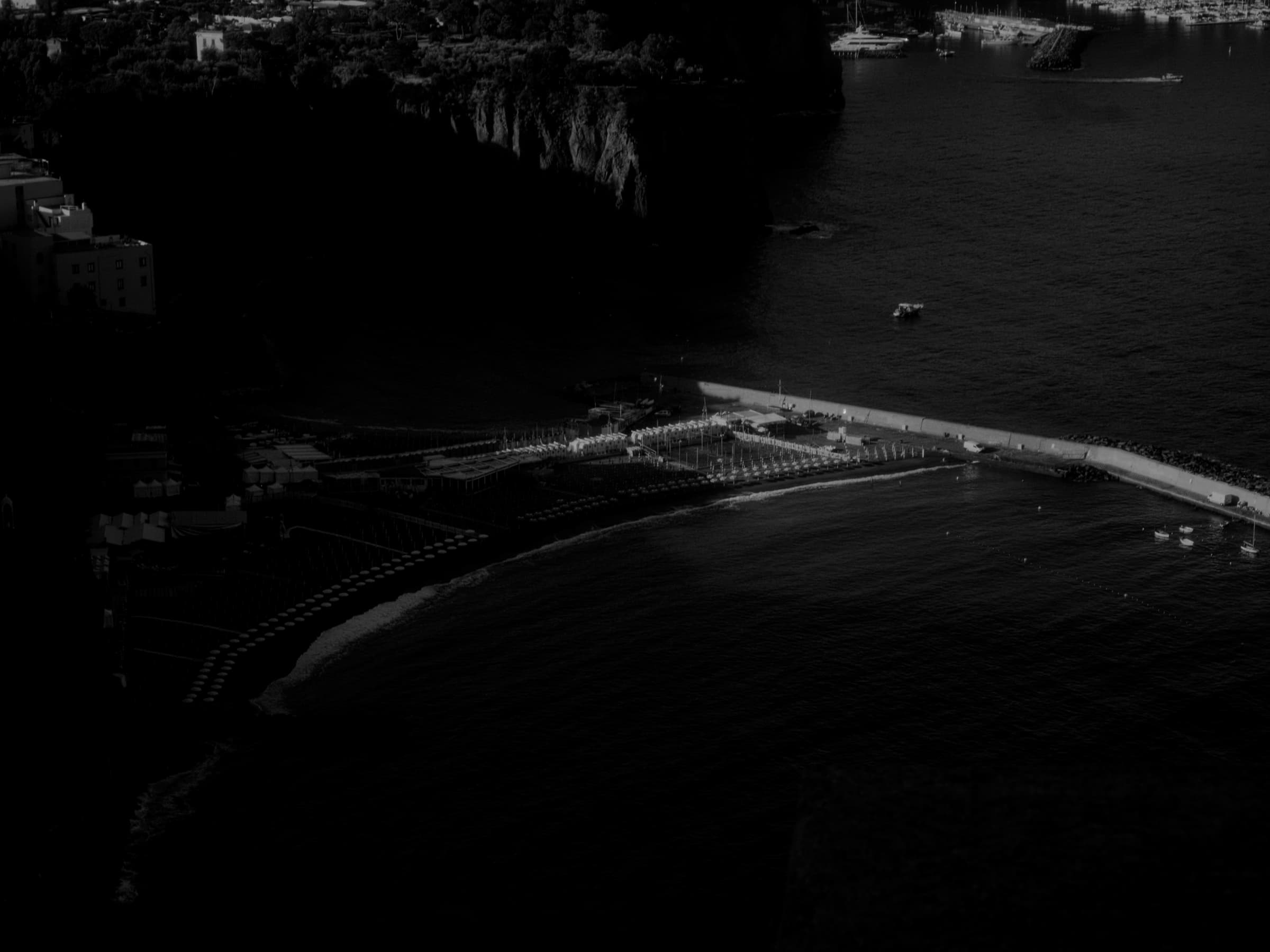 A coastline and harbor seen from above, with a pier and small boats.