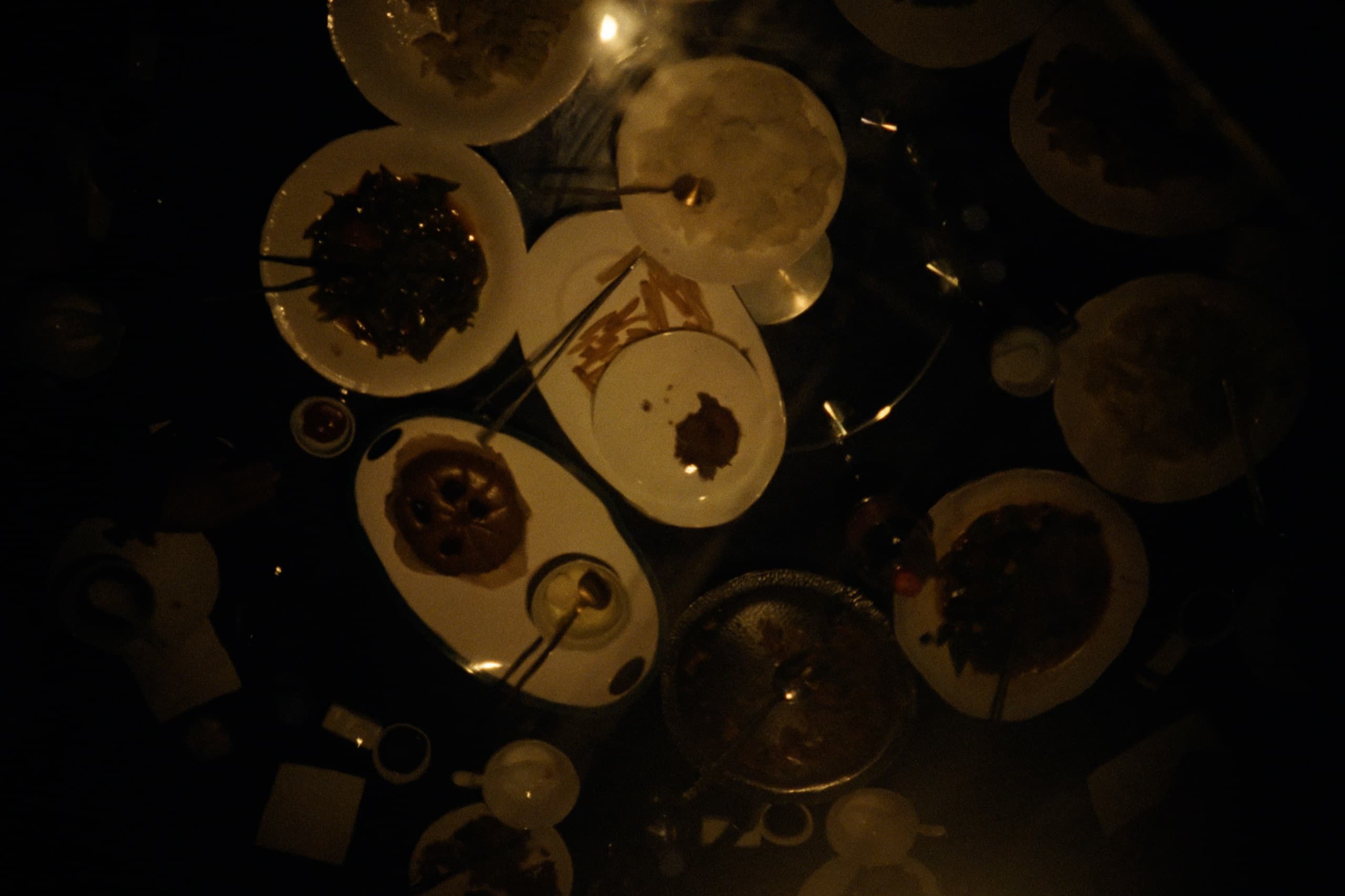 Overhead view of a dinner table covered in plates of Chinese food, chopsticks, and glasses in dim warm light.