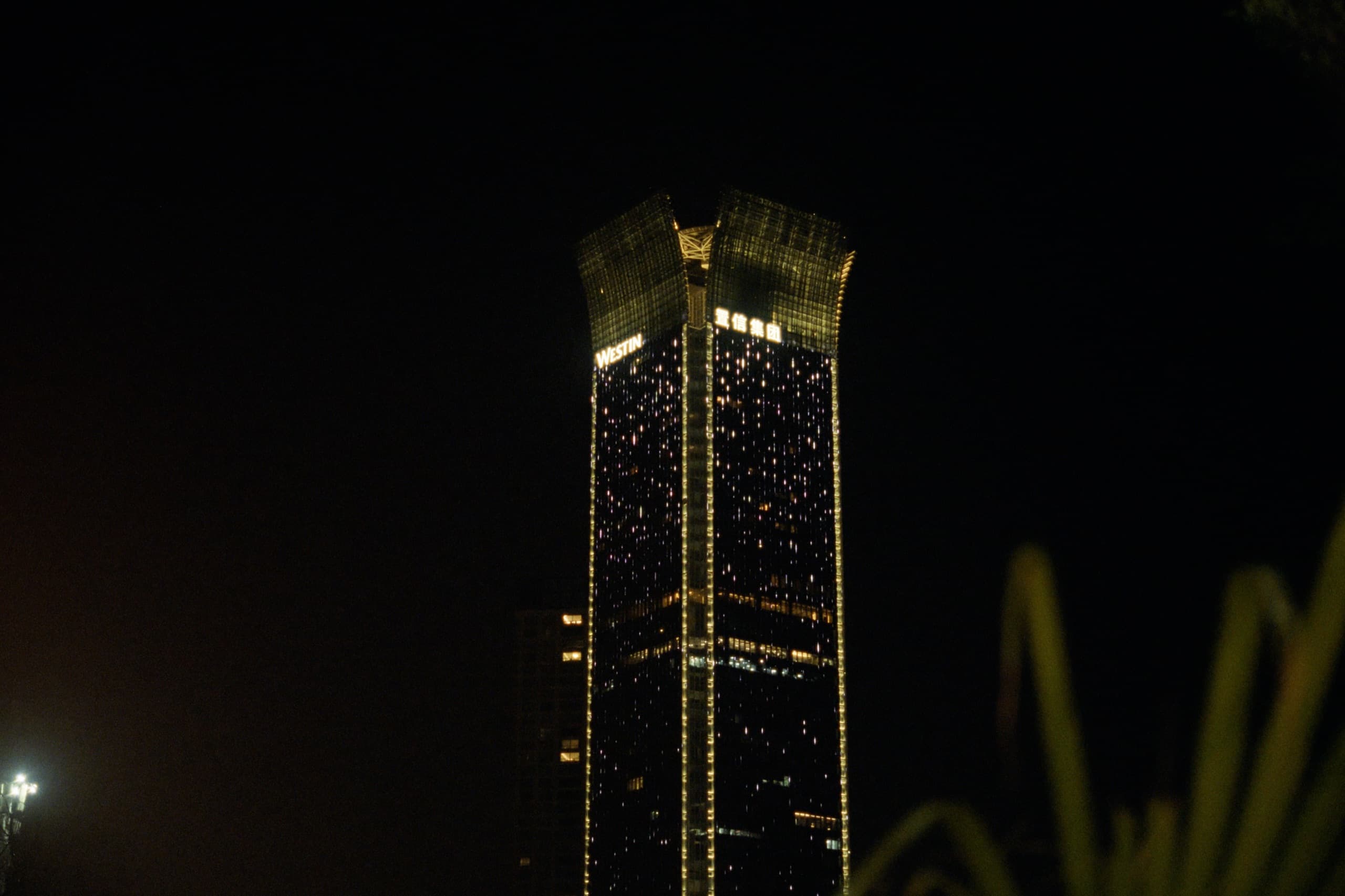 A tall Westin hotel tower illuminated with golden lights against a black night sky, Chinese characters glowing near the top.