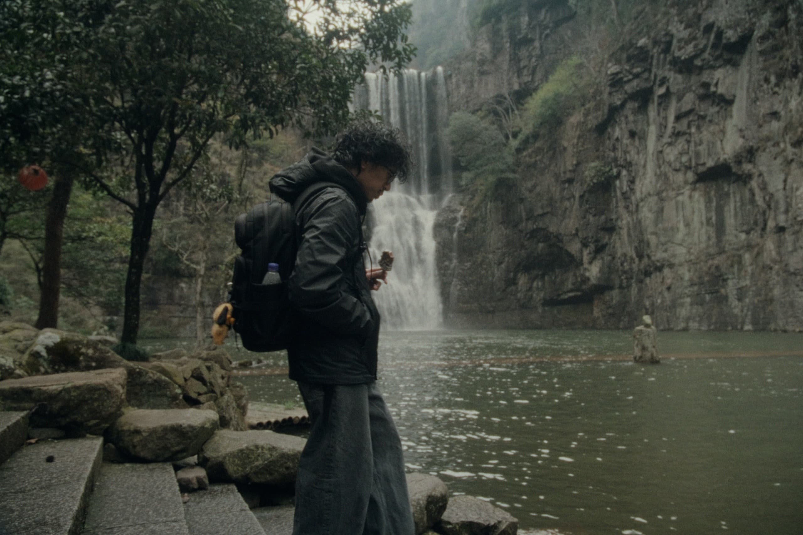 Andrew in profile on stone steps at the edge of a pool, a waterfall cascading down a rocky cliff behind him.