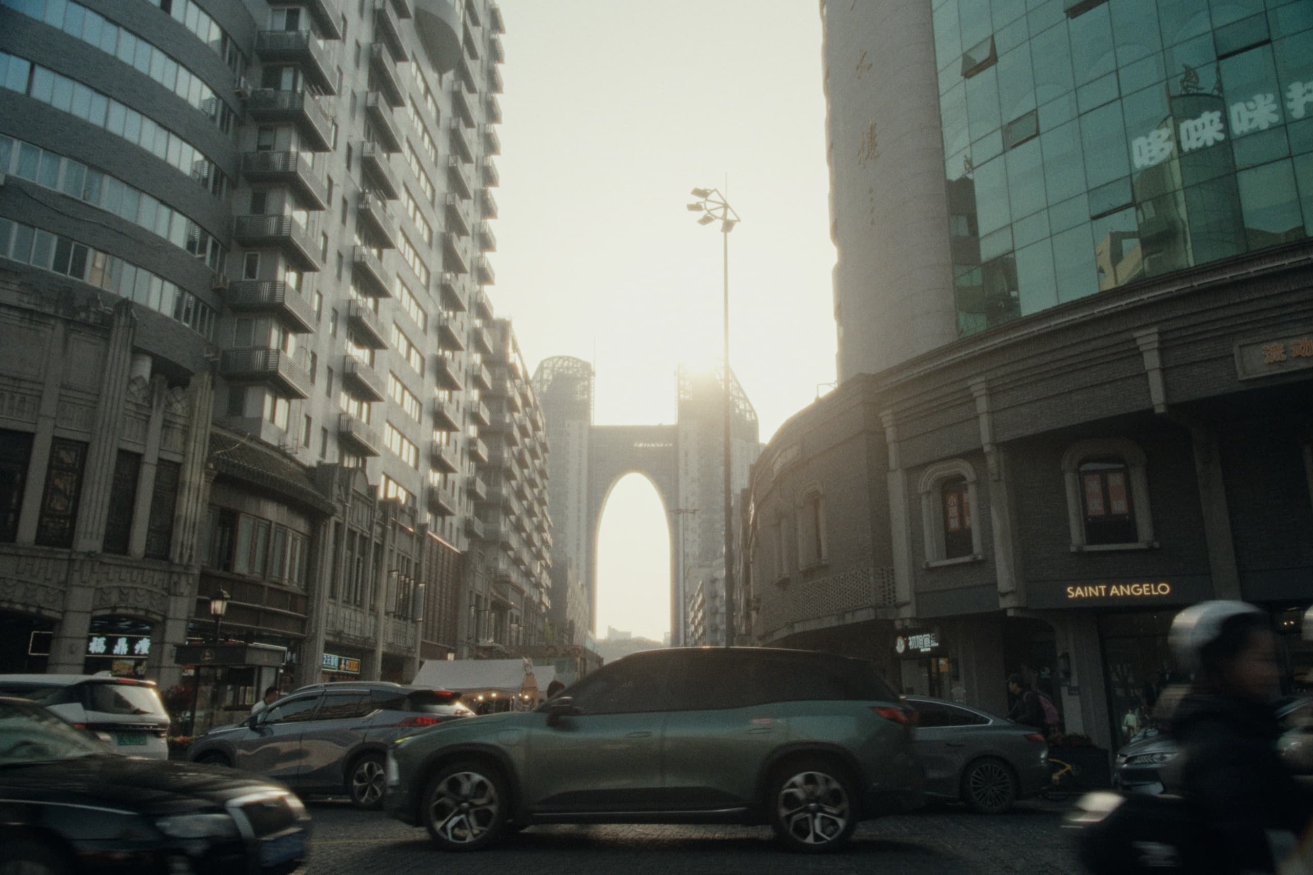 A busy Wenzhou street at golden hour with traffic, scooters, and storefronts framing a massive arch-shaped skyscraper glowing in the haze.