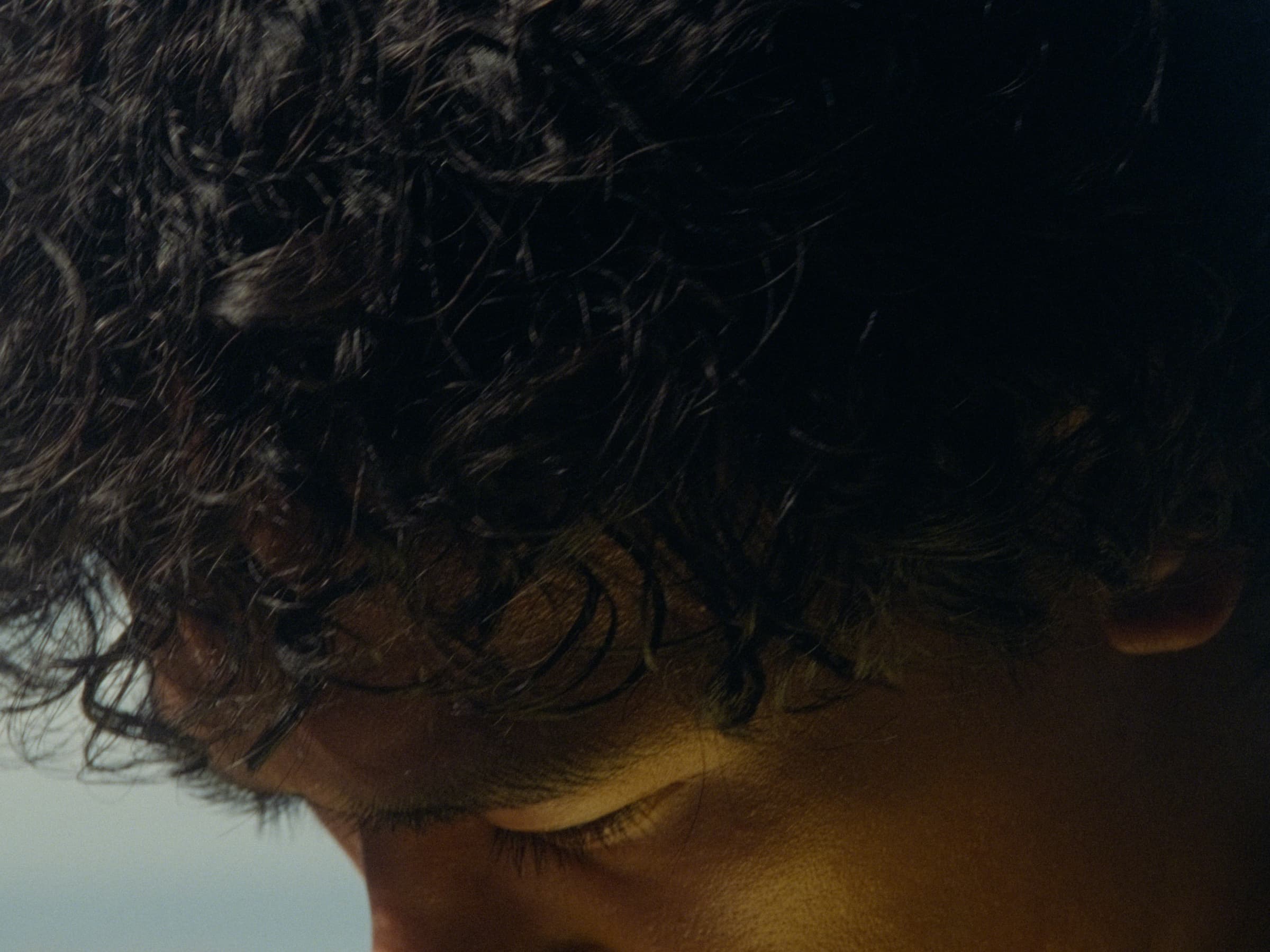 Andrew Amisola in White Sands in Boracay — Extreme close-up of dark curls and a downward-cast eye warmed by golden sidelight.