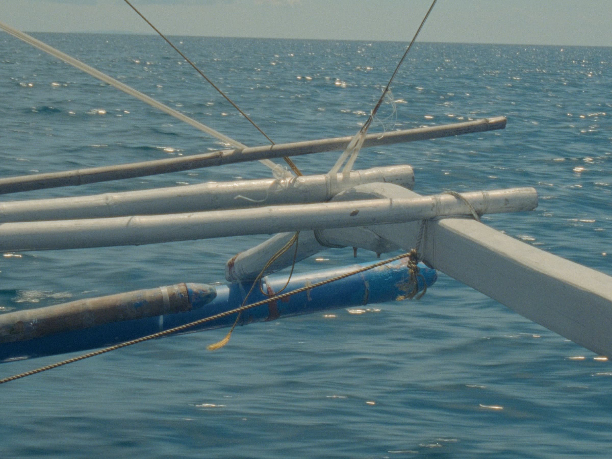 Detail of a parked paraw's bamboo outrigger and crossbeams resting on the calm blue sea.