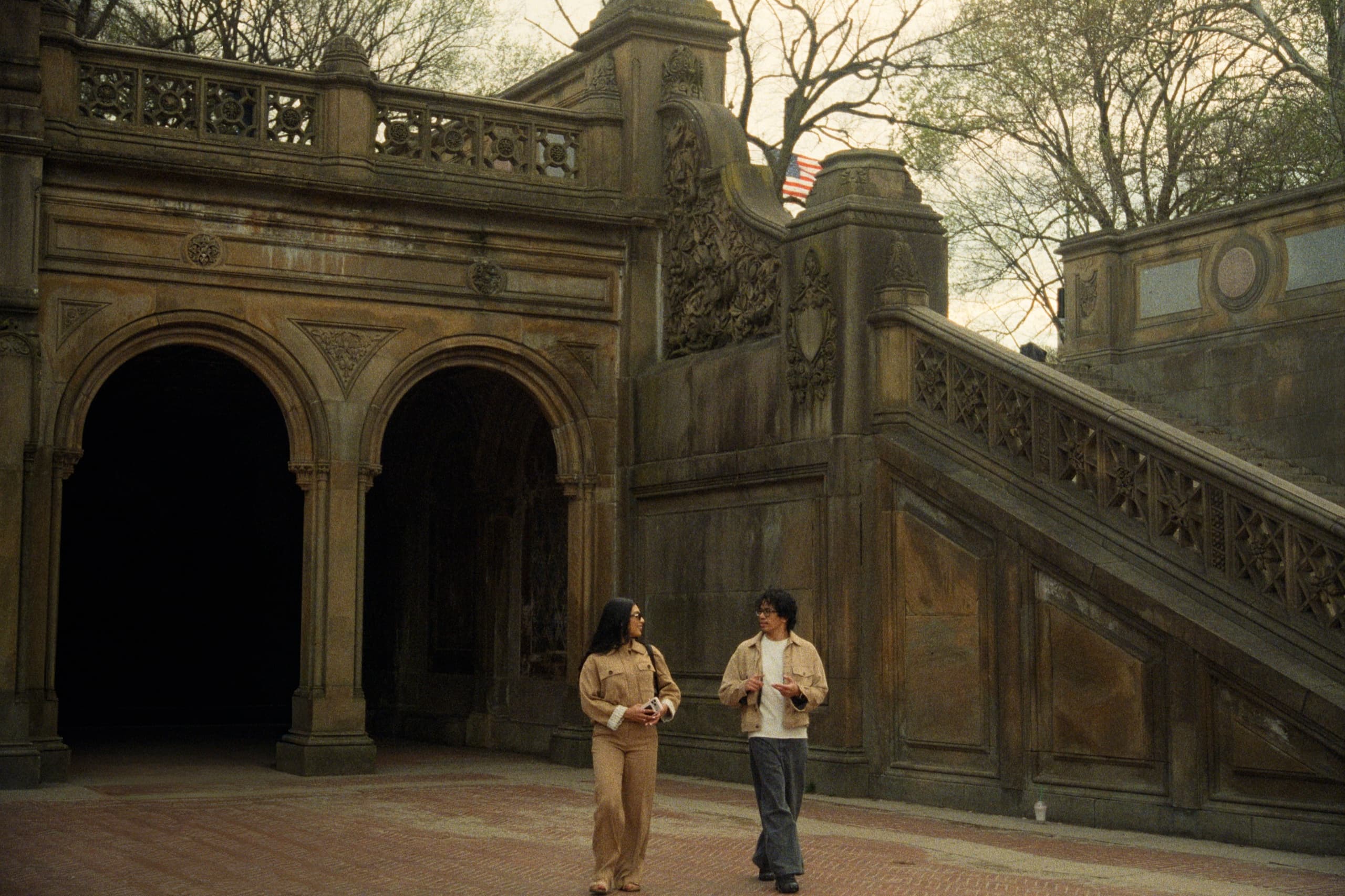 Andrew and Jackie walking together at Bethesda Terrace in Central Park with ornate stonework and staircase behind them