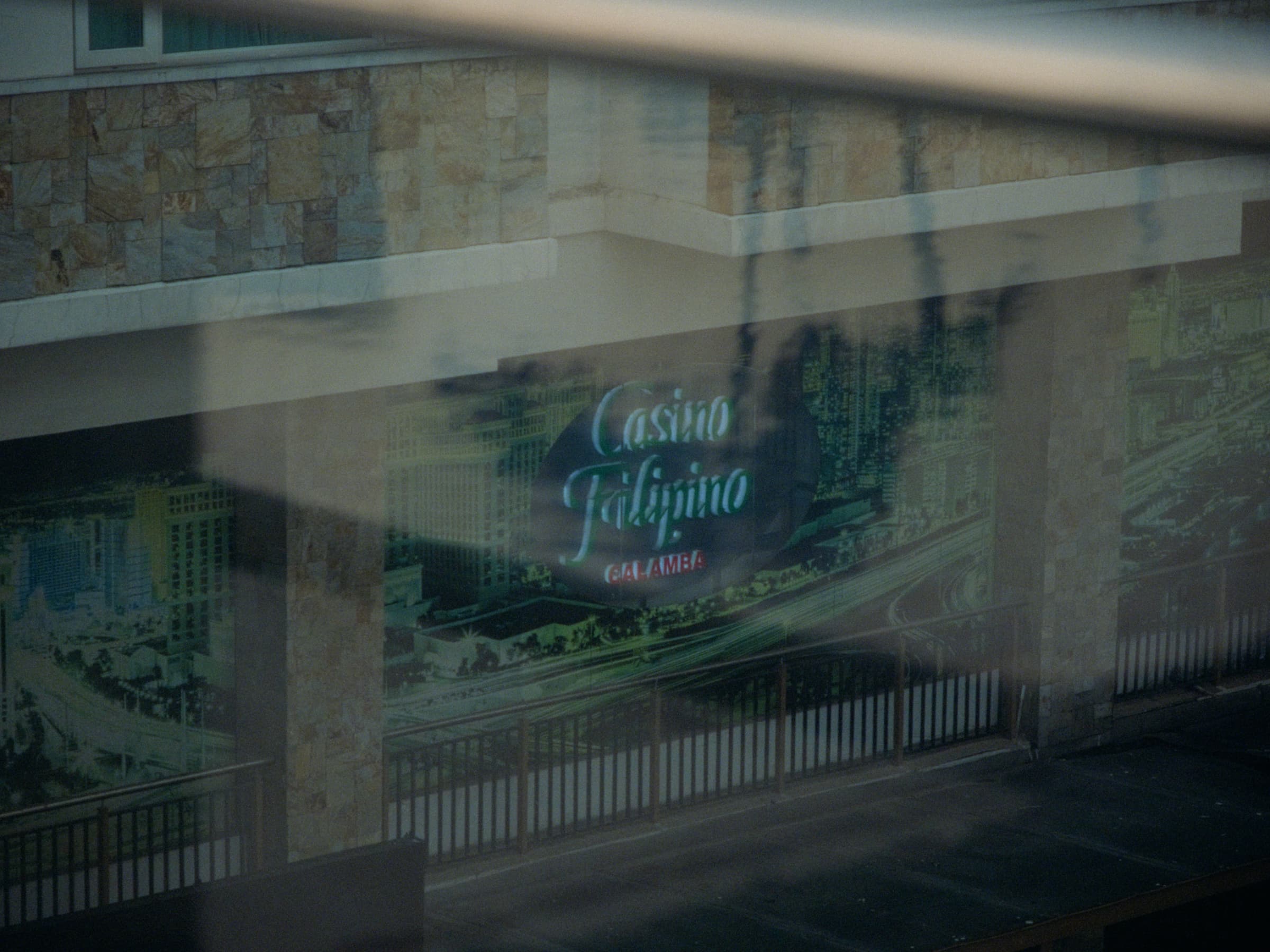 A Casino Filipino Calamba mural-and-signage panel seen reflected through layered glass at twilight
