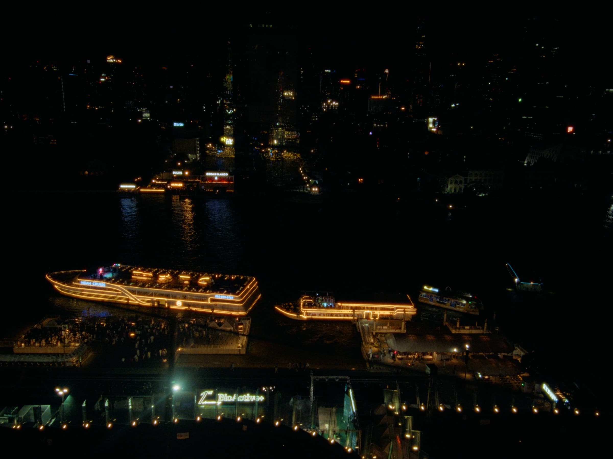 Lit cruise boats docked along the Chao Phraya River at night with Bangkok's skyline glittering across the water