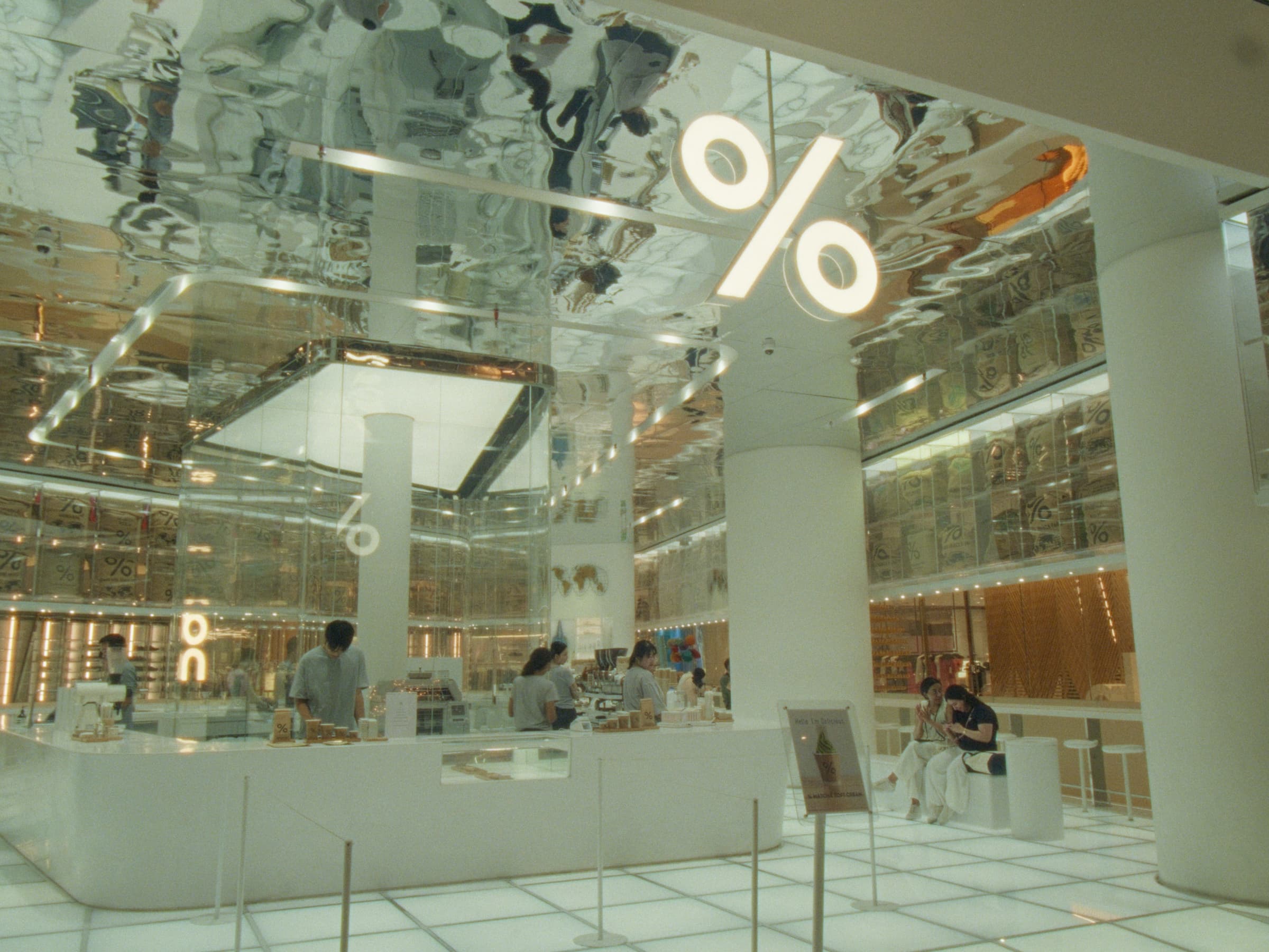 The interior of a % Arabica café with a mirrored ceiling reflecting the white counter and shoppers below
