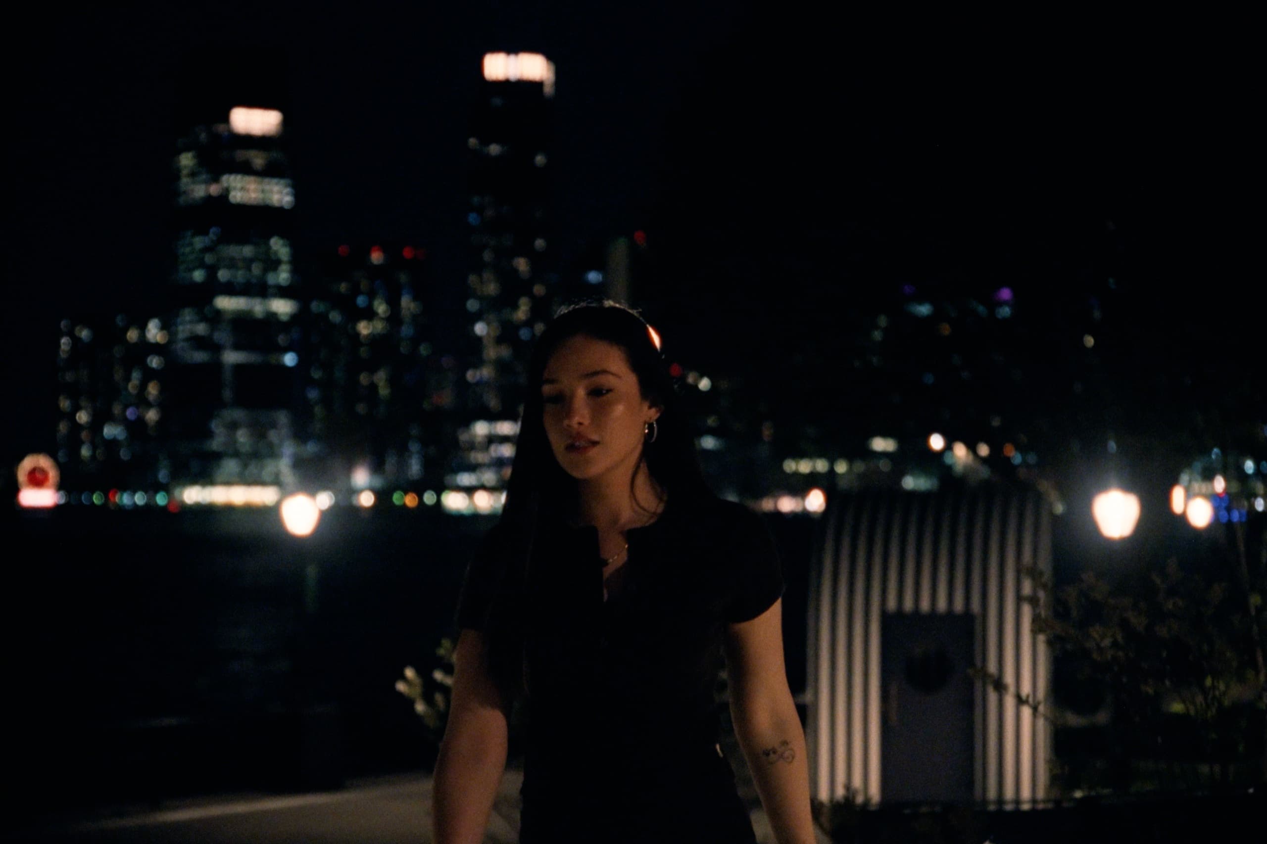 Juliana walking at night with city skyline bokeh glowing behind her