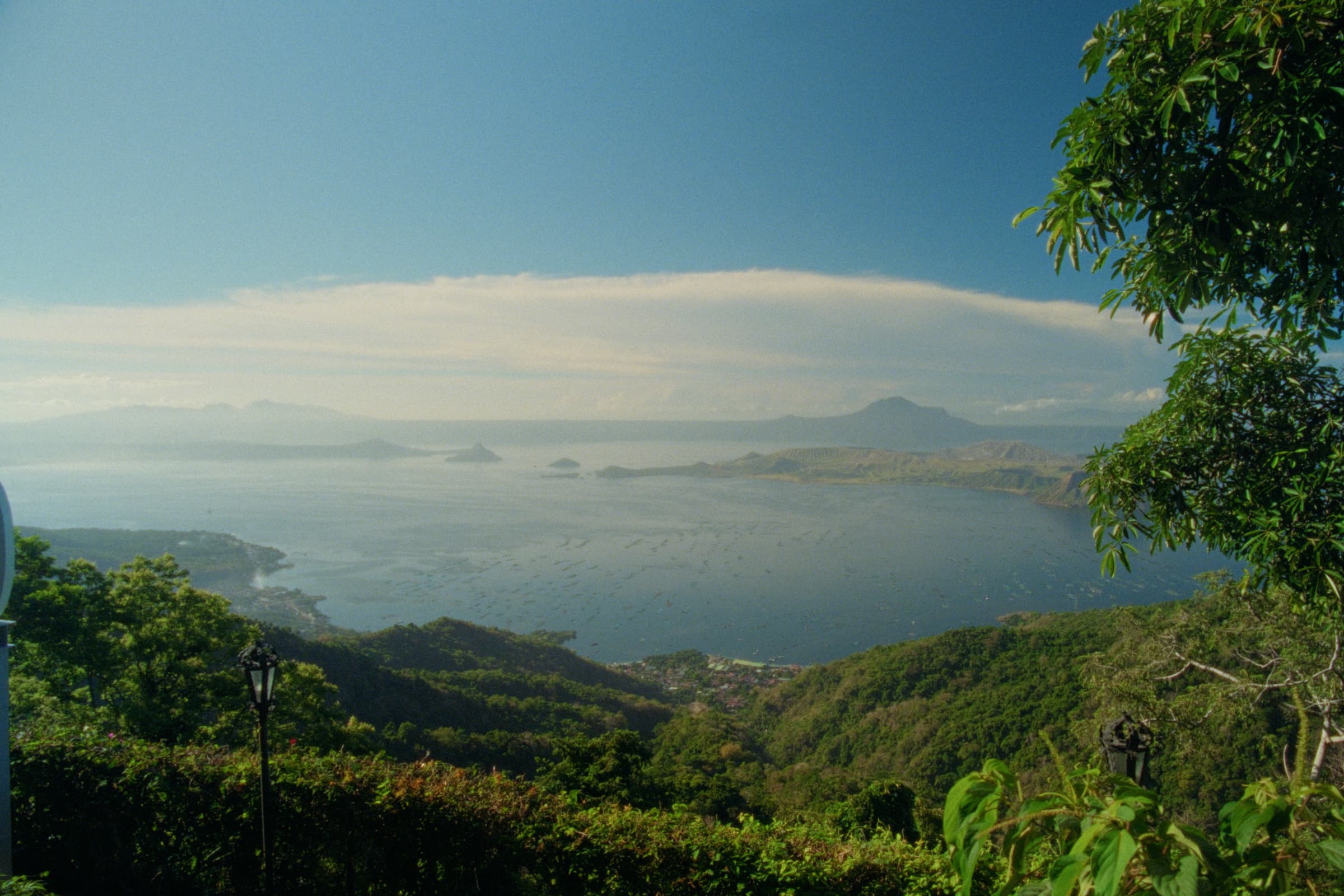A wide view of Taal Lake and the volcano caldera from Tagaytay, with a curving shoreline of fish pens