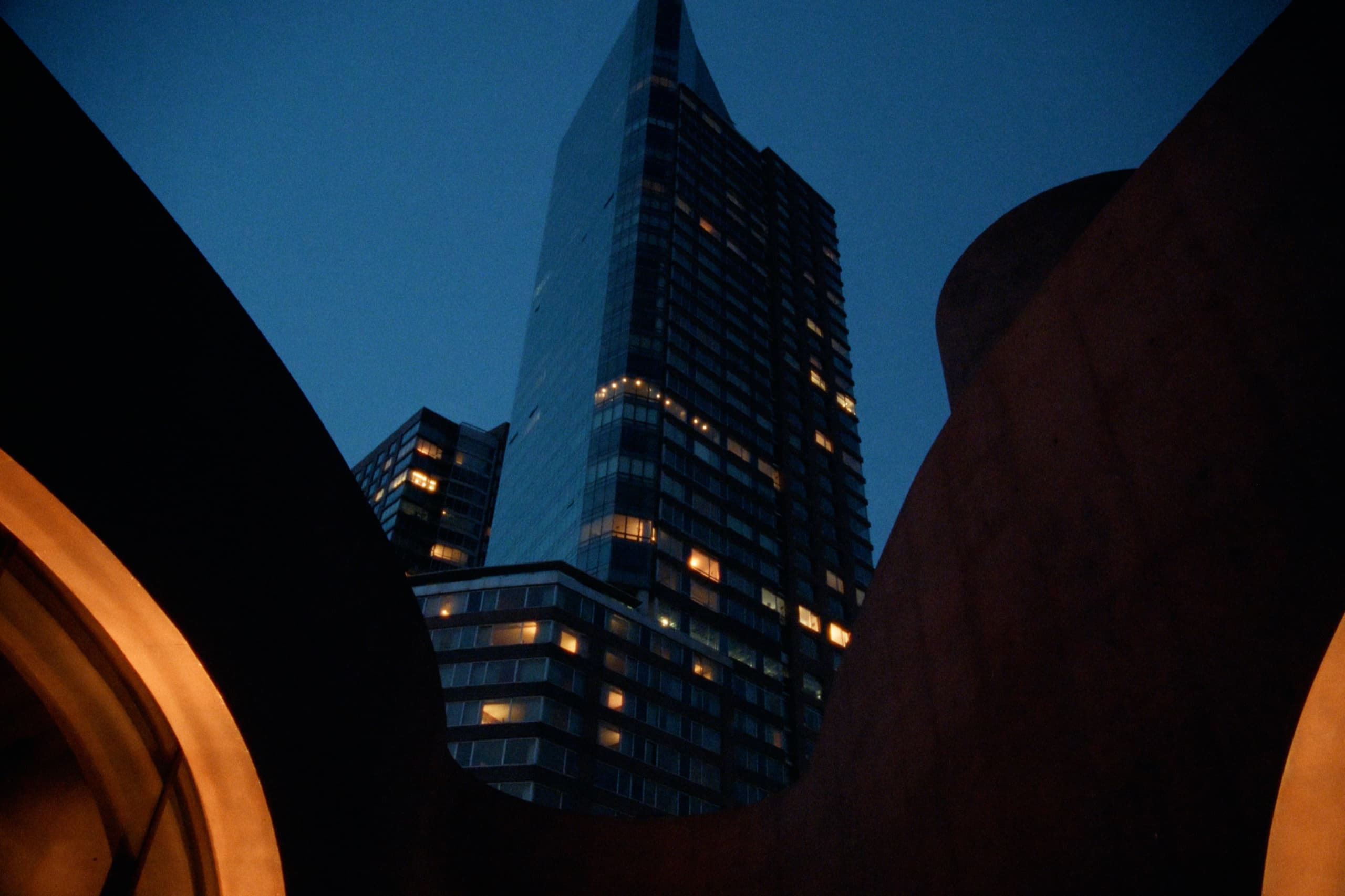 Glass skyscraper framed through dark sculptural arches with warm amber light at night
