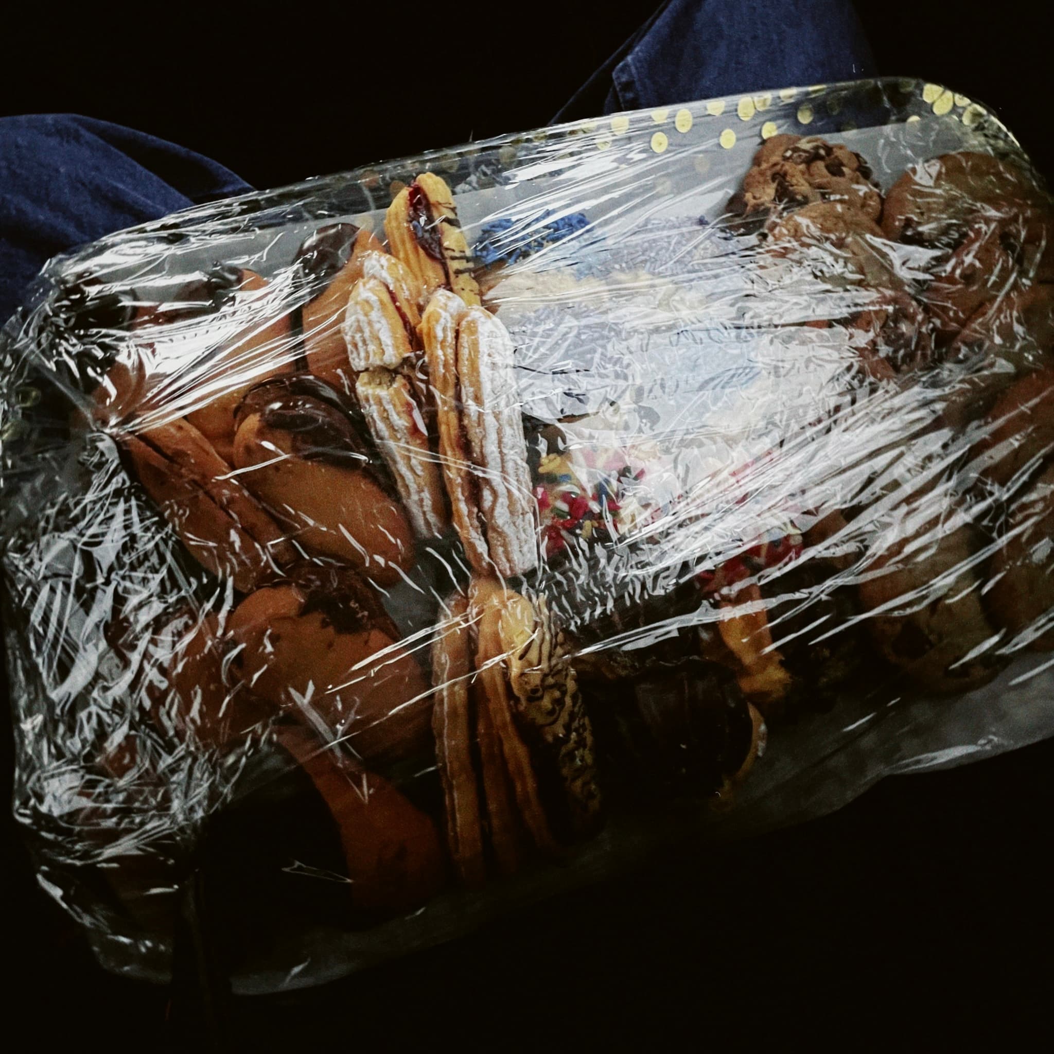 A plate of cookies wrapped in plastic, sitting in someone's lap in darkness—brought to a family gathering on the day everything changed