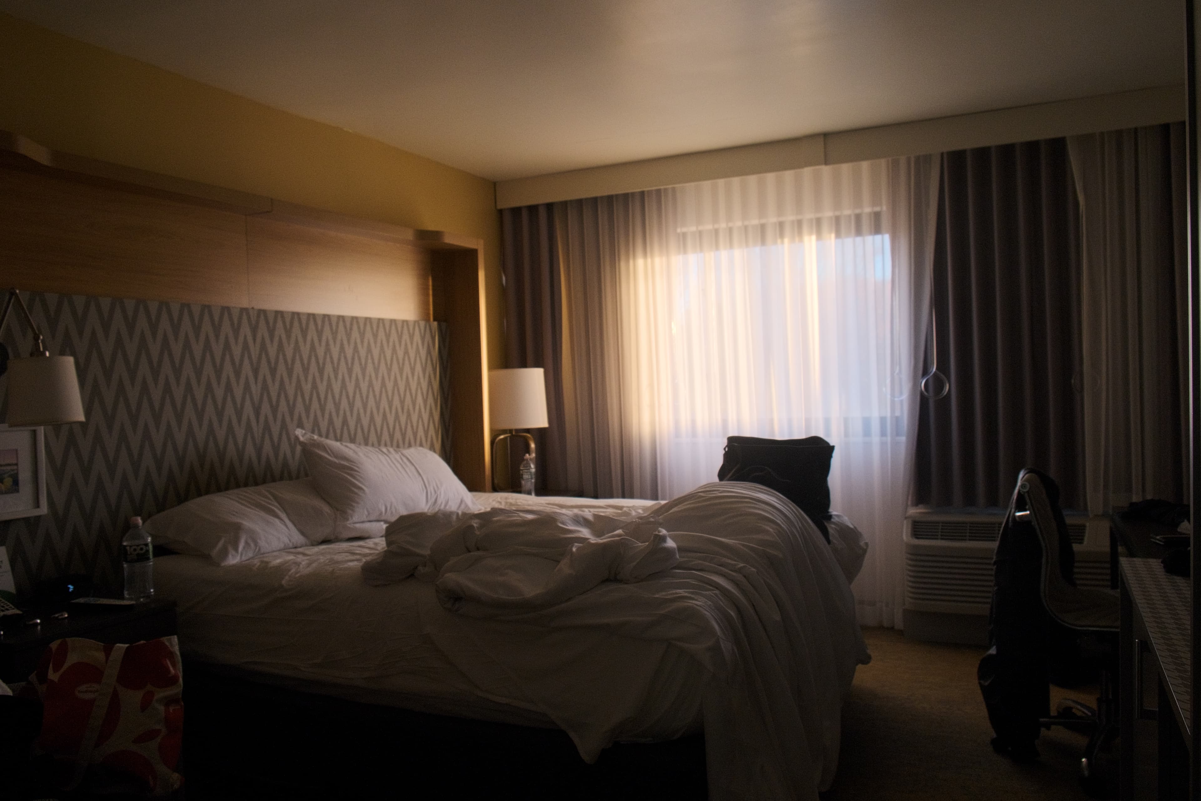 Hotel room, unmade bed, light through blinds